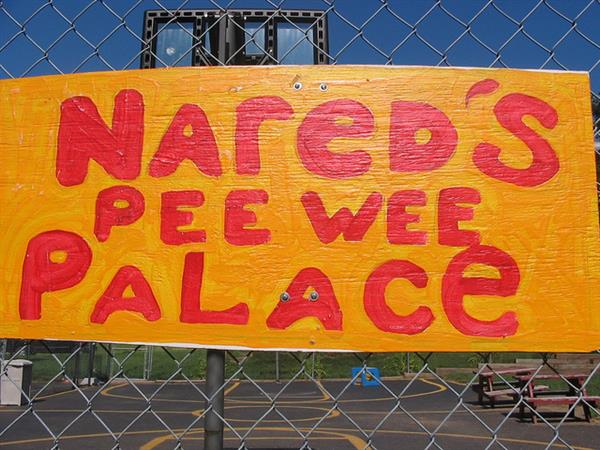 Handpainted sign for Nared's Pee Wee Palace attached to chainlink fence around a basketball court